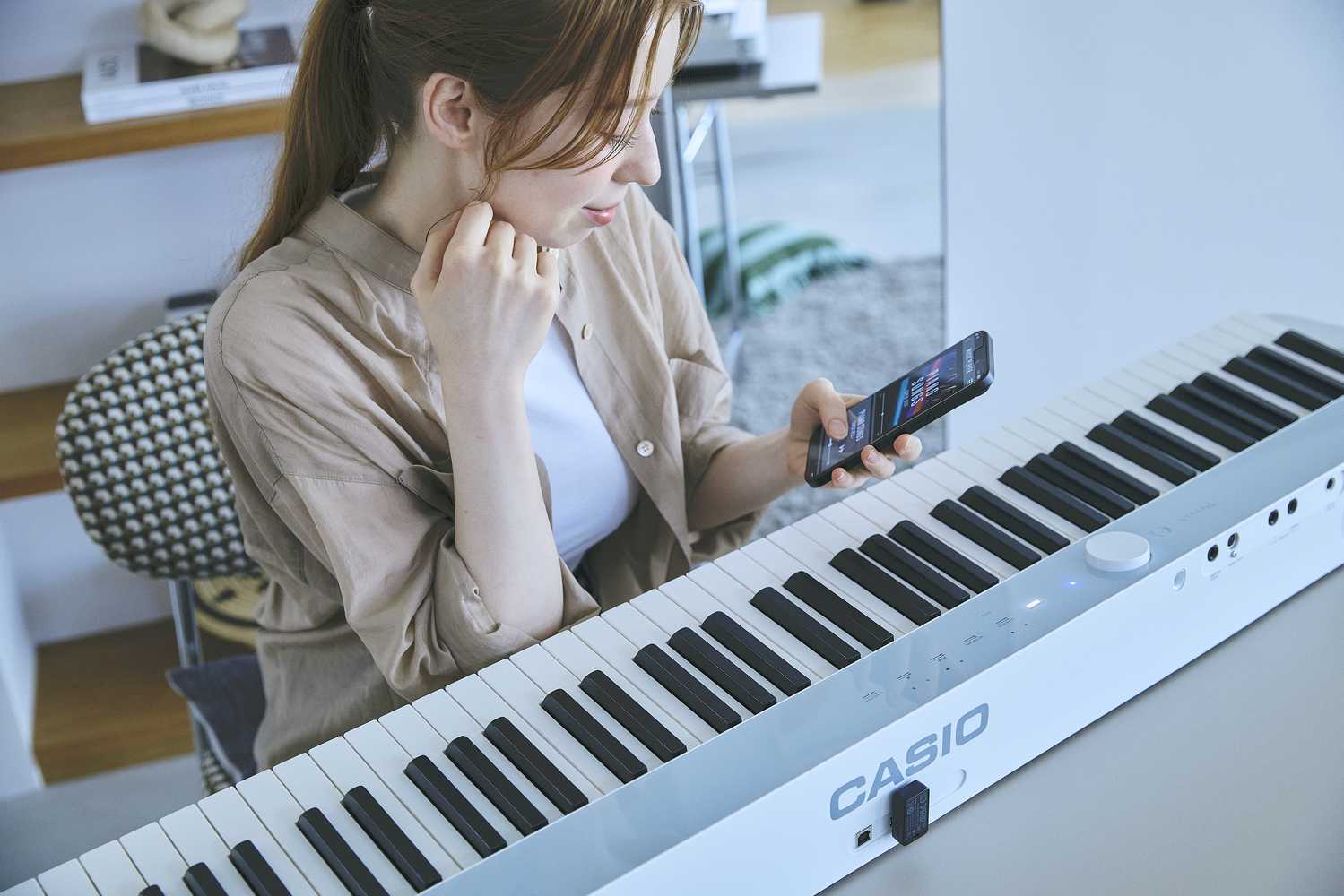 Casio Privia PX-S1100CB mobile Casio Privia PX-S1100CB Lifestyle Frau mit Smartphone sitzt beim Piano
